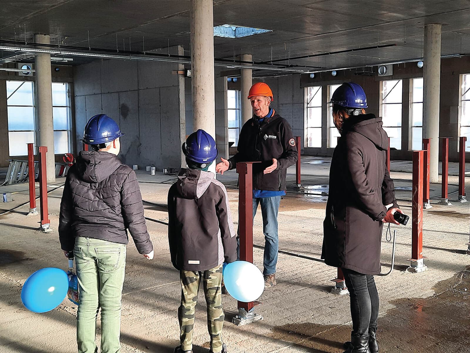 Kinderen met bouwhelmen krijgen uitleg op de bouwplaats
